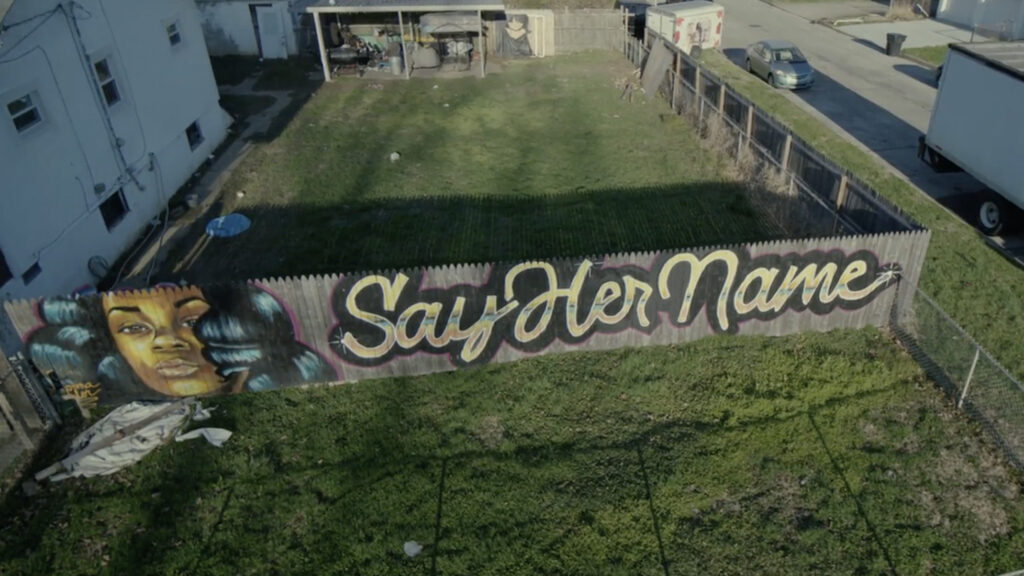 Aerial shot of fence with 'Say Her Name' painted on it